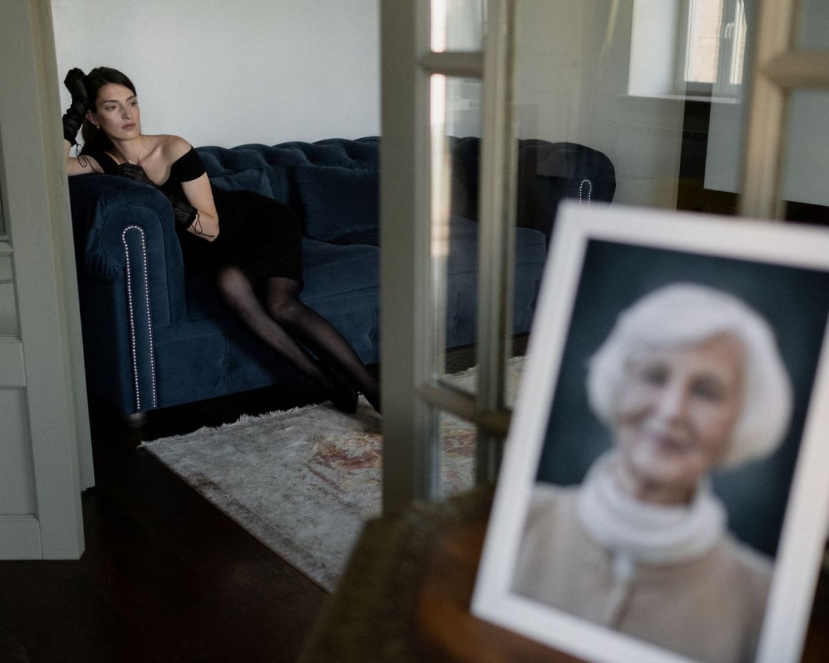 Frau sitzt auf dem Sofa und im Vordergrund steht ein Bild von ihrer Oma, verschwommen.