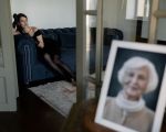 Frau sitzt auf dem Sofa und im Vordergrund steht ein Bild von ihrer Oma, verschwommen.