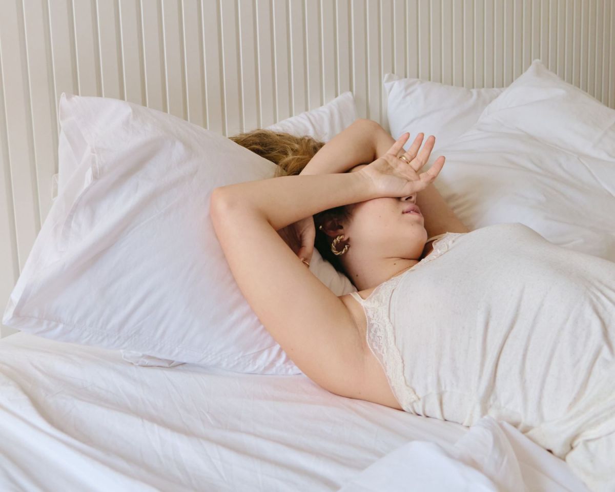 Frau im Bett hält sich einen Arm vors Gesicht, weil ihr warm ist