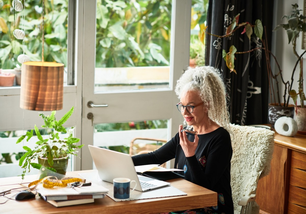 Grauhaarige Frau arbeitet zu Hause am Laptop.