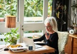 Grauhaarige Frau arbeitet zu Hause am Laptop.