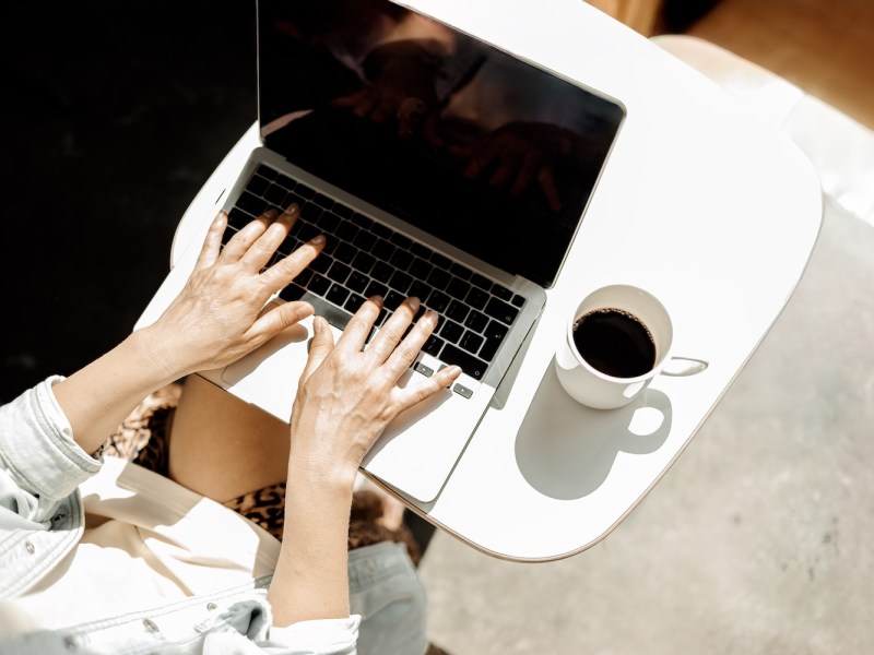 Eine reife Frau mittleren Alters arbeitet remote mit einem Laptop und Kaffee.