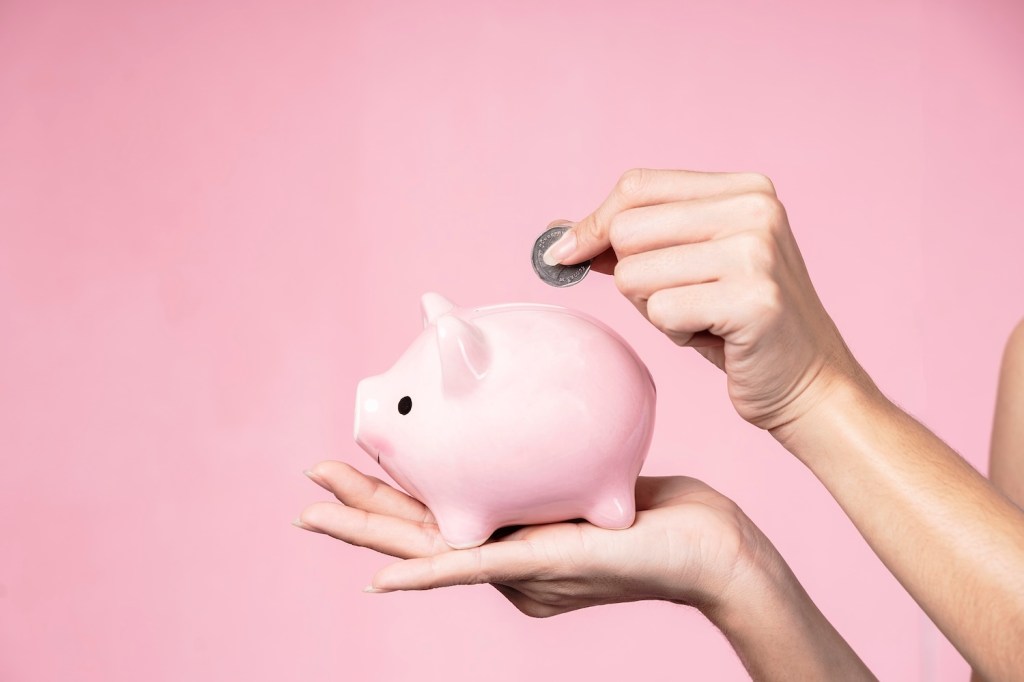 Nahaufnahme von Händen, die Münzen in ein Sparschwein werfen.