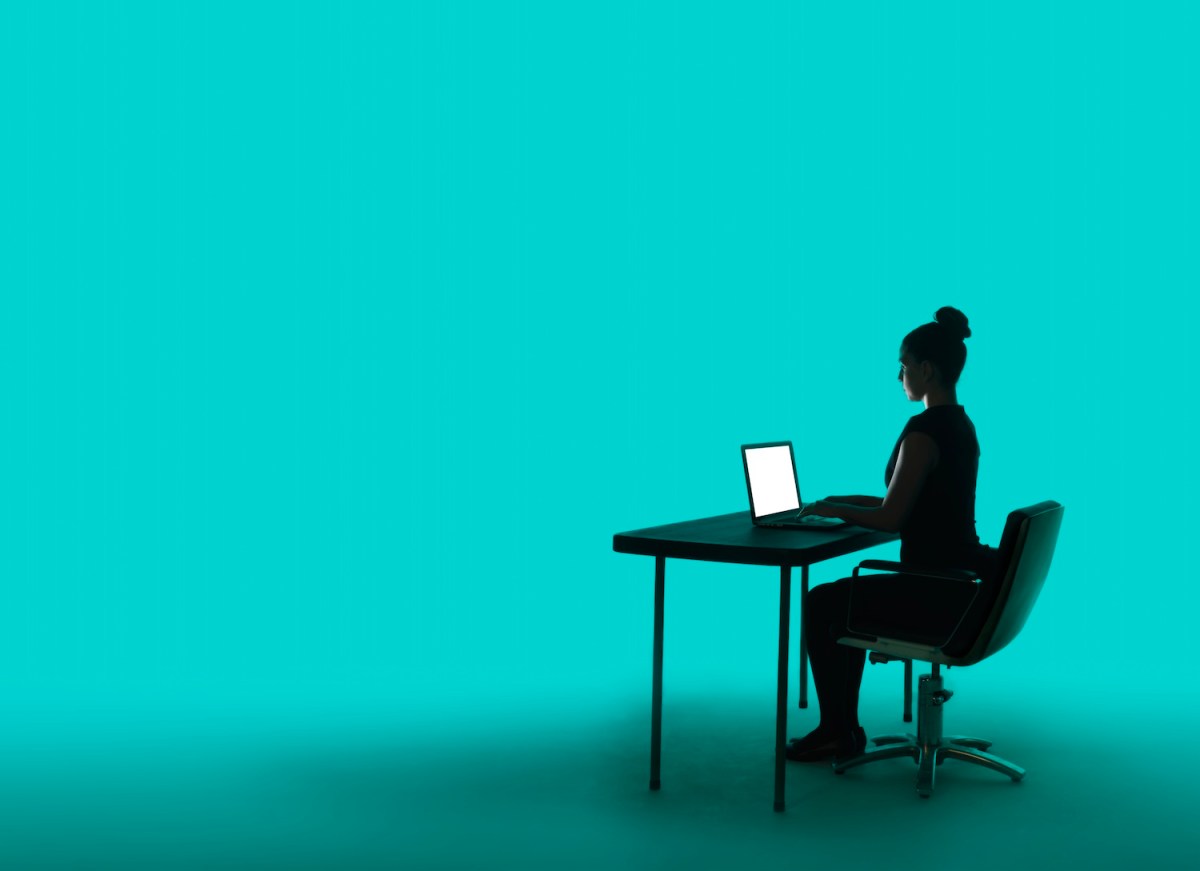 Junge Geschäftsfrau in Silhouette, sitzt an ihrem Schreibtisch mit beleuchtetem Laptop, auf kräftigem türkisfarbenem Hintergrund.