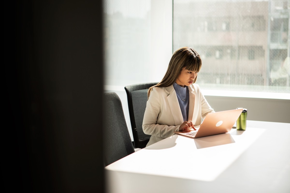 Eine Frau im Anzug sitzt im Büro und arbeitet am Laptop.