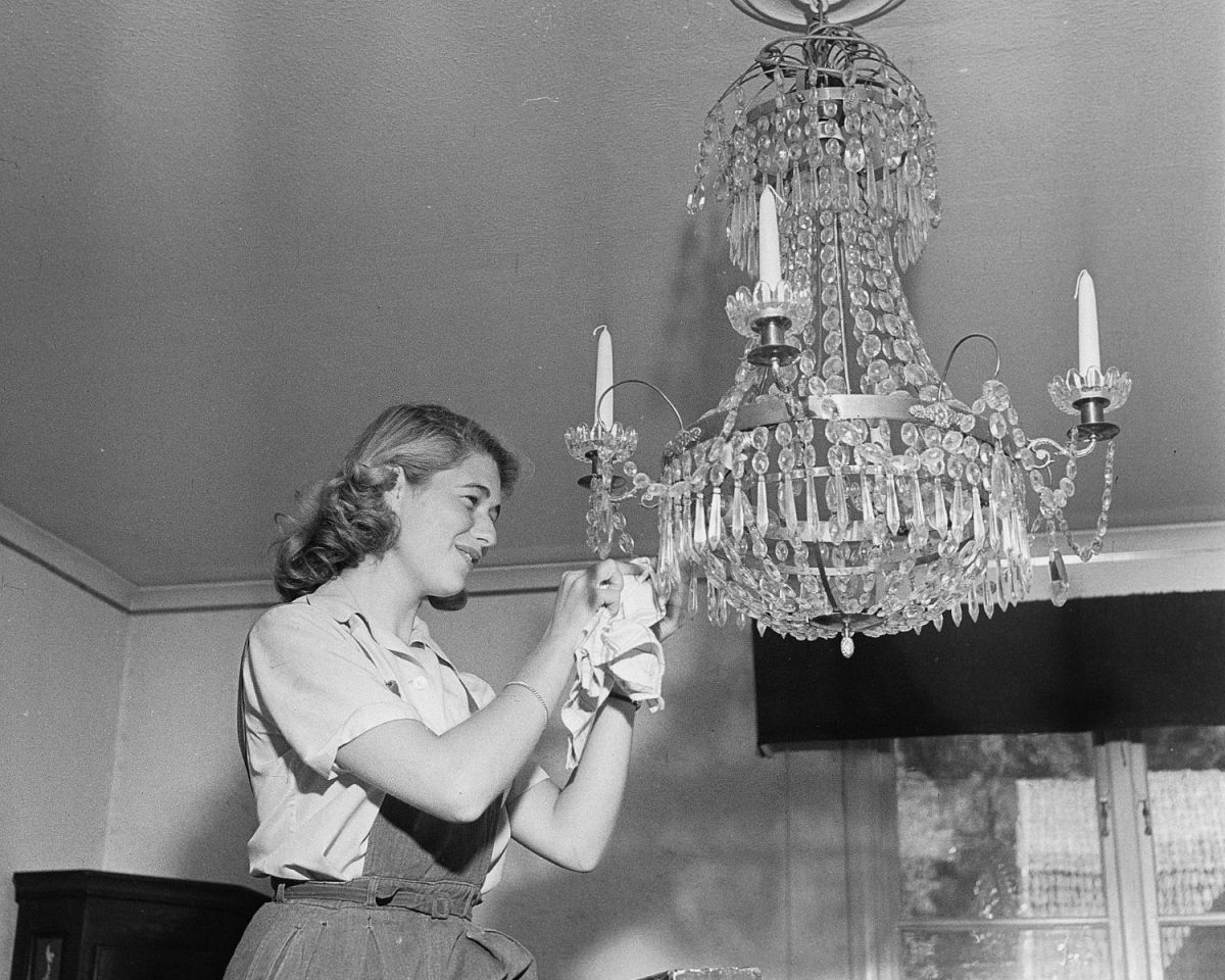 Frau putzt einen Kronleuchter.