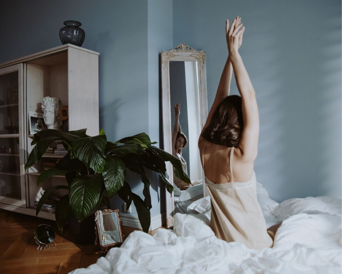 Frau streckt sich im Bett neben einer Zimmerpflanze