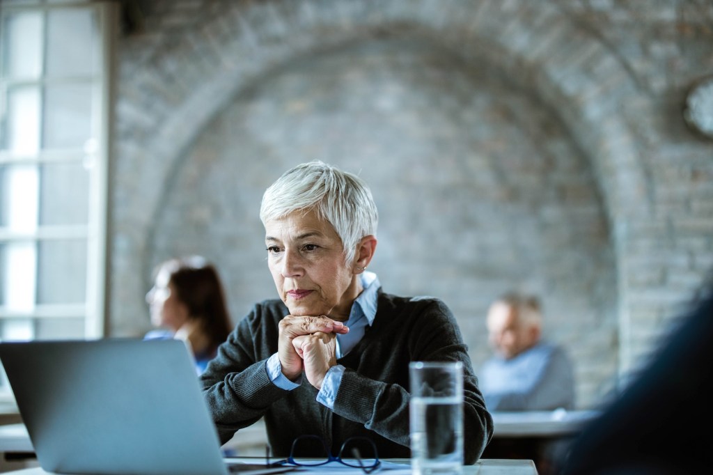 Eine ältere Dame mit grauen kurzen Haaren arbeitet in einem Büro.