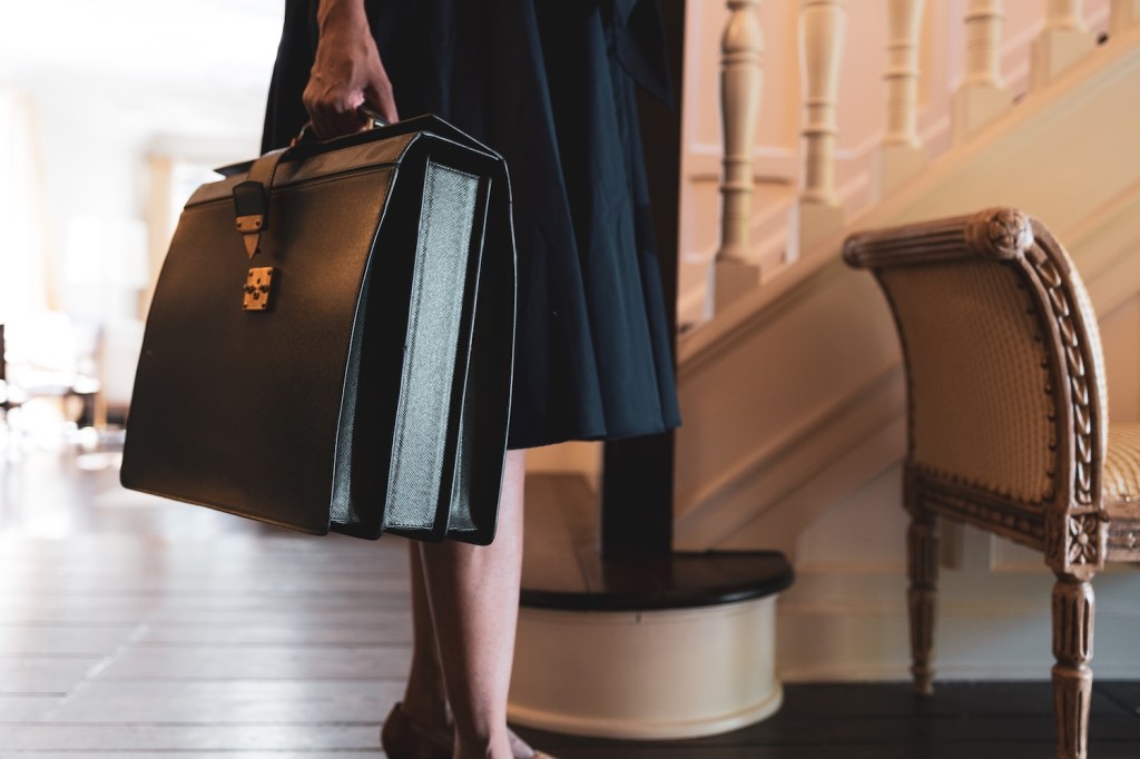 Gut gekleidete, berufstätige Frau trägt eine Aktentasche in der Hand.