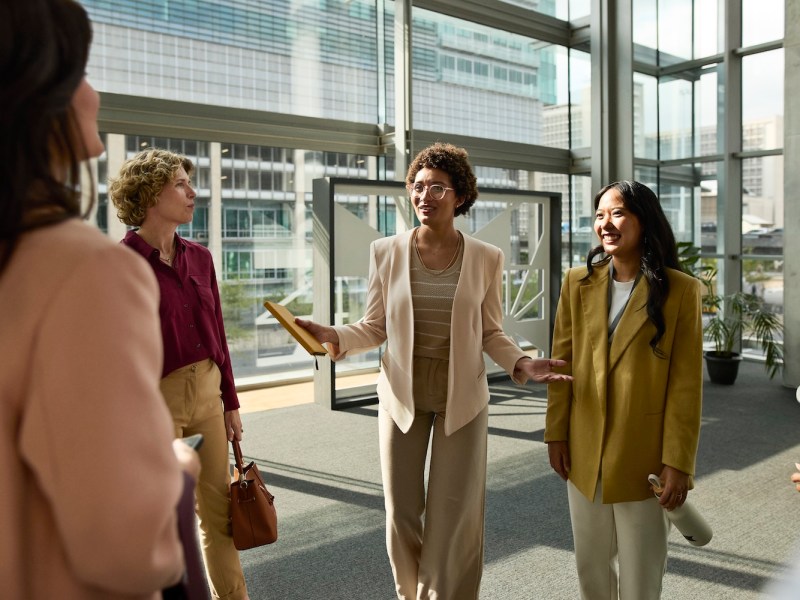 Lächelnde Geschäftsfrau interagiert mit Kollegen, die in der Bürolobby stehen.