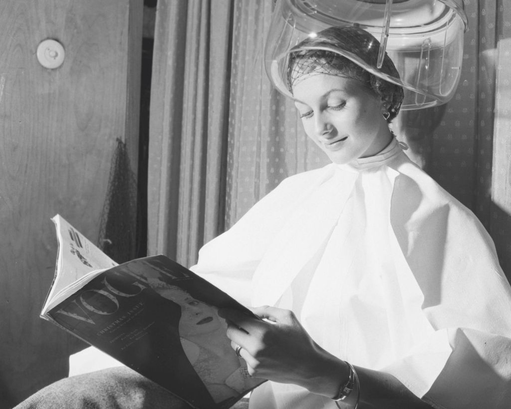 Frau unter einer Friseur-Haube mit einer alten Vogue-Zeitschrift in der Hand.