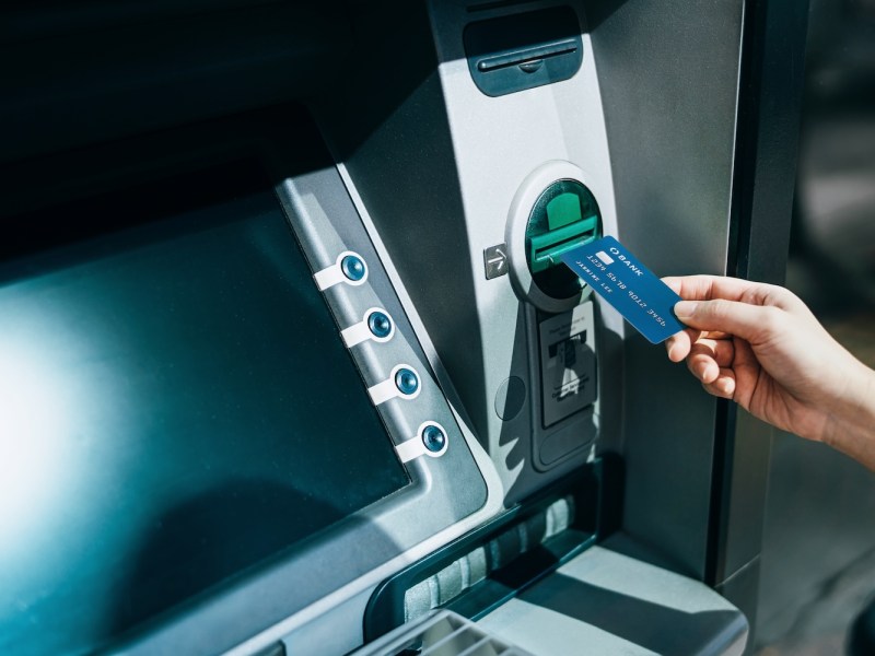 Eine Frauenhand führt eine Bankkarte in einen Geldautomaten ein, um Geld abzuheben.