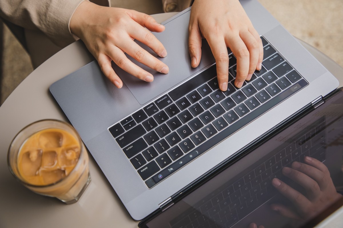 Draufsicht auf eine Frauenhand, die in einem Café einen Laptop benutzt.