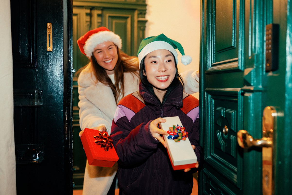 Freundinnen mit festlichen Hüten kommen an der Tür an und halten verpackte Geschenke in der Hand.