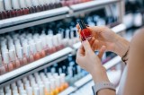 Nahaufnahme einer jungen Frau, die in einem Kosmetikgeschäft einkauft und Nagellack aus einem Regal auswählt.