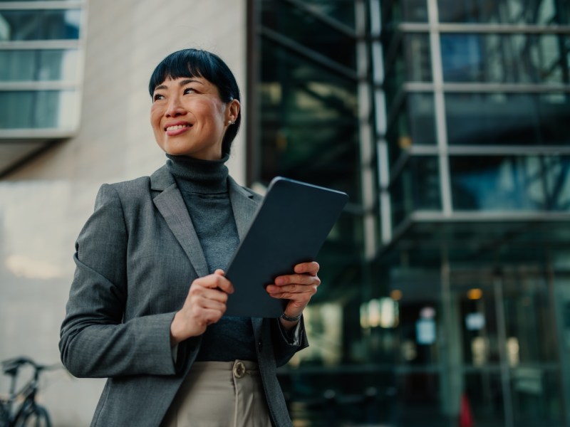 Eine glückliche Geschäftsfrau hält ein Tablet in der Hand und schaut weg.