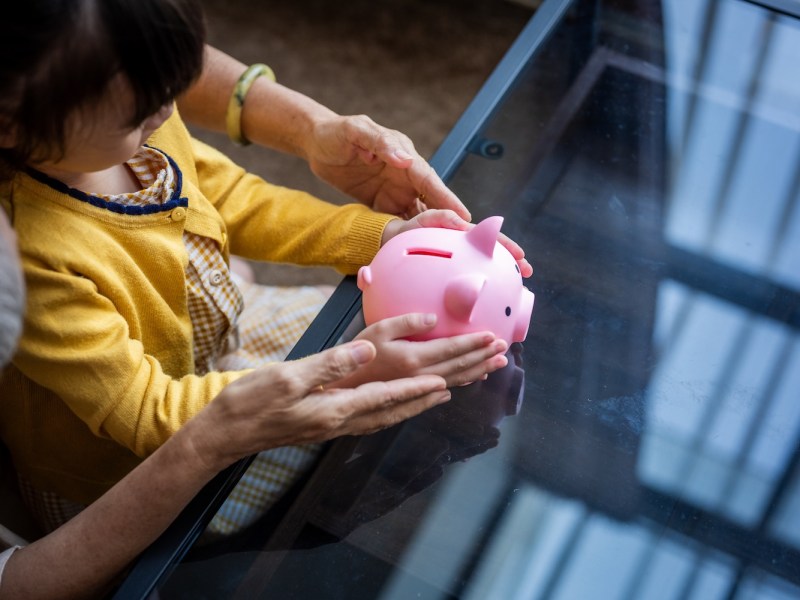 Ein kleines Mädchen und ihre Mutter halten zu Hause ein rosa Sparschwein in den Händen.