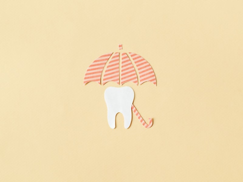 Zahn unter einem Regenschirm auf gelbem Hintergrund.